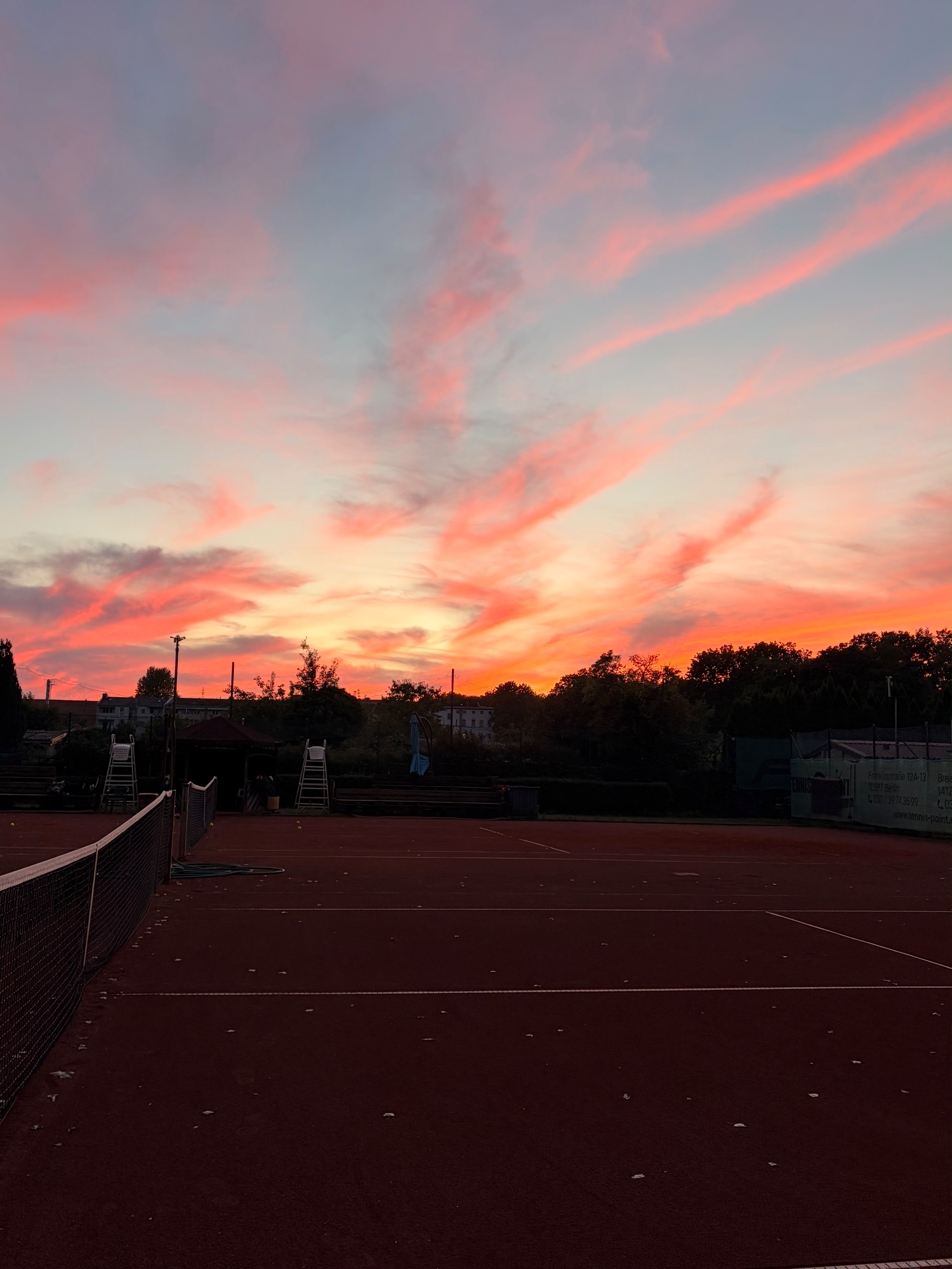 Empty clay tennis courts framed by a fiery sunset