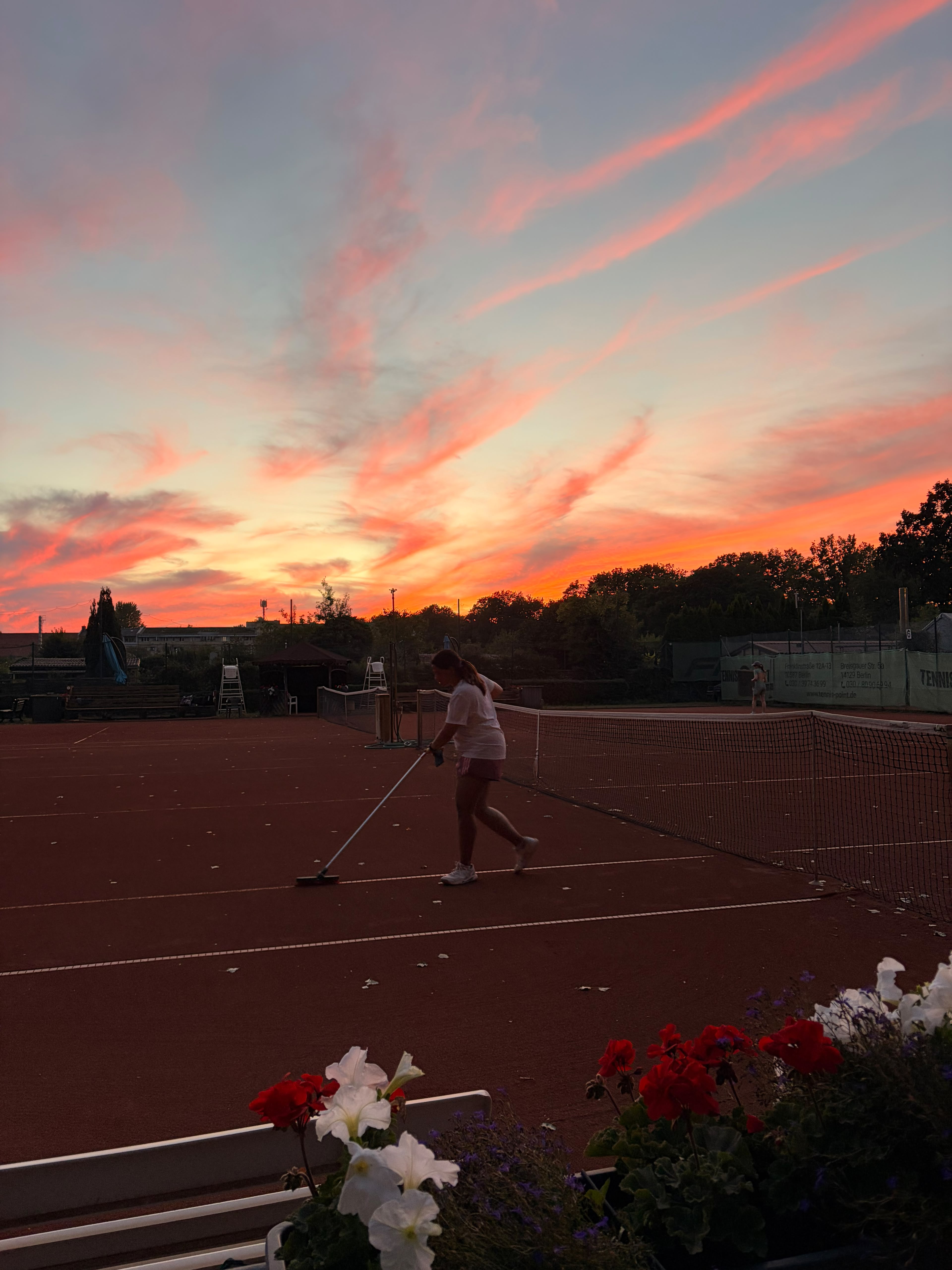 A player sweeping the clay court under a glowing sunset sky